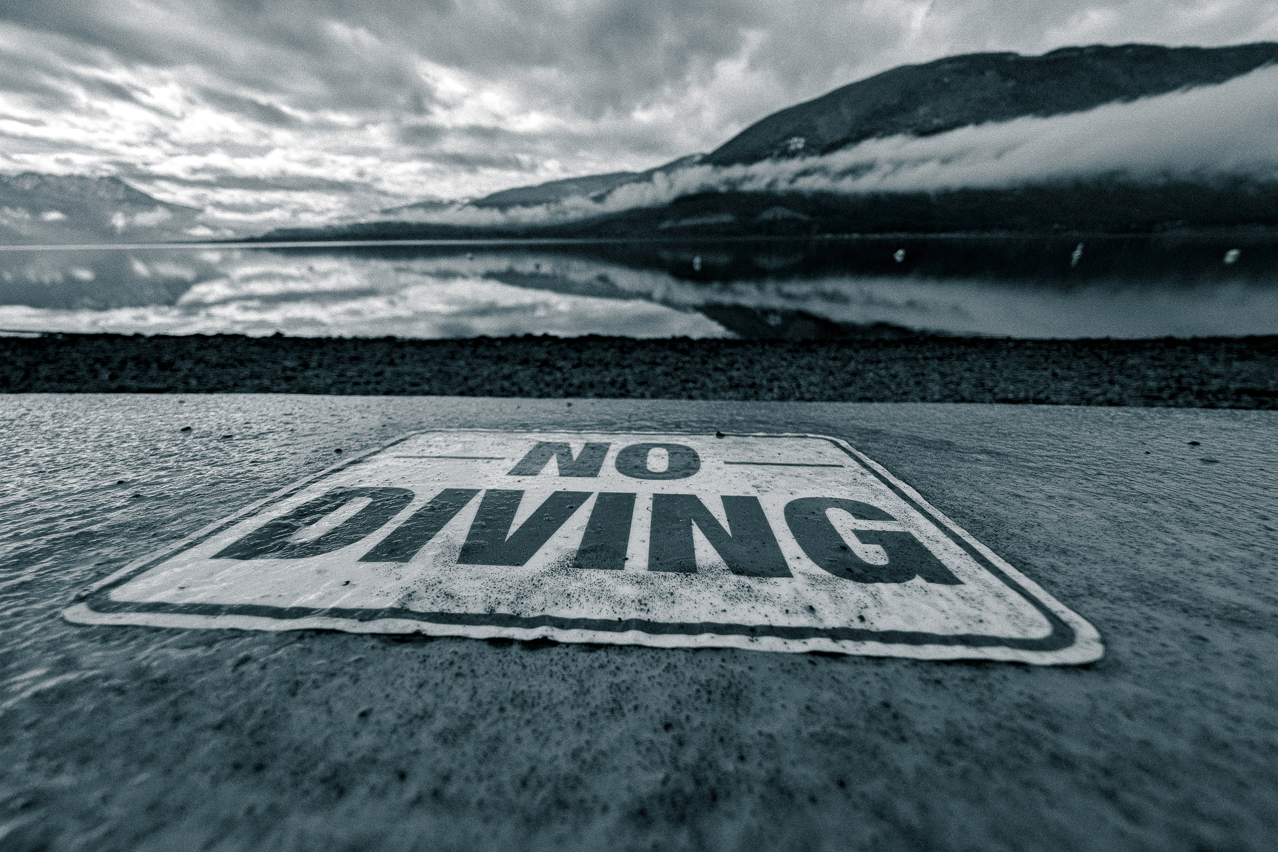 A large no-diving warning is painted across a lakeside surface beneath low clouds.