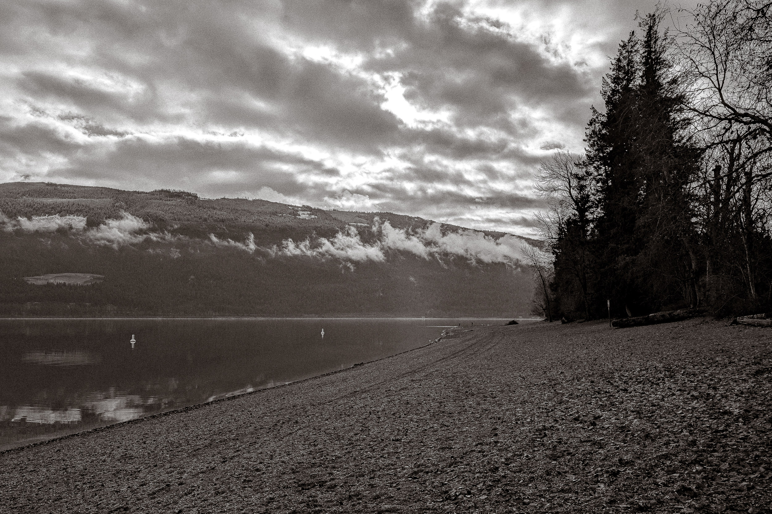 Clouds break over a quiet lake and a dark tree-lined shore.
