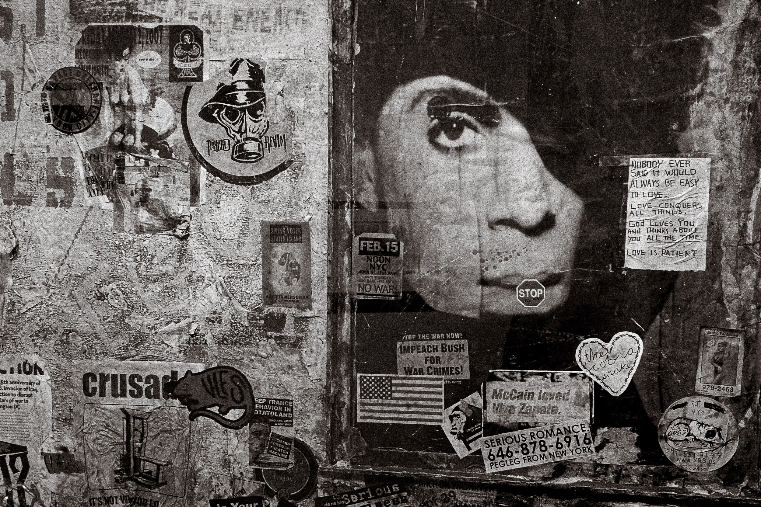 A painted face and layered posters cover a weathered outdoor wall.