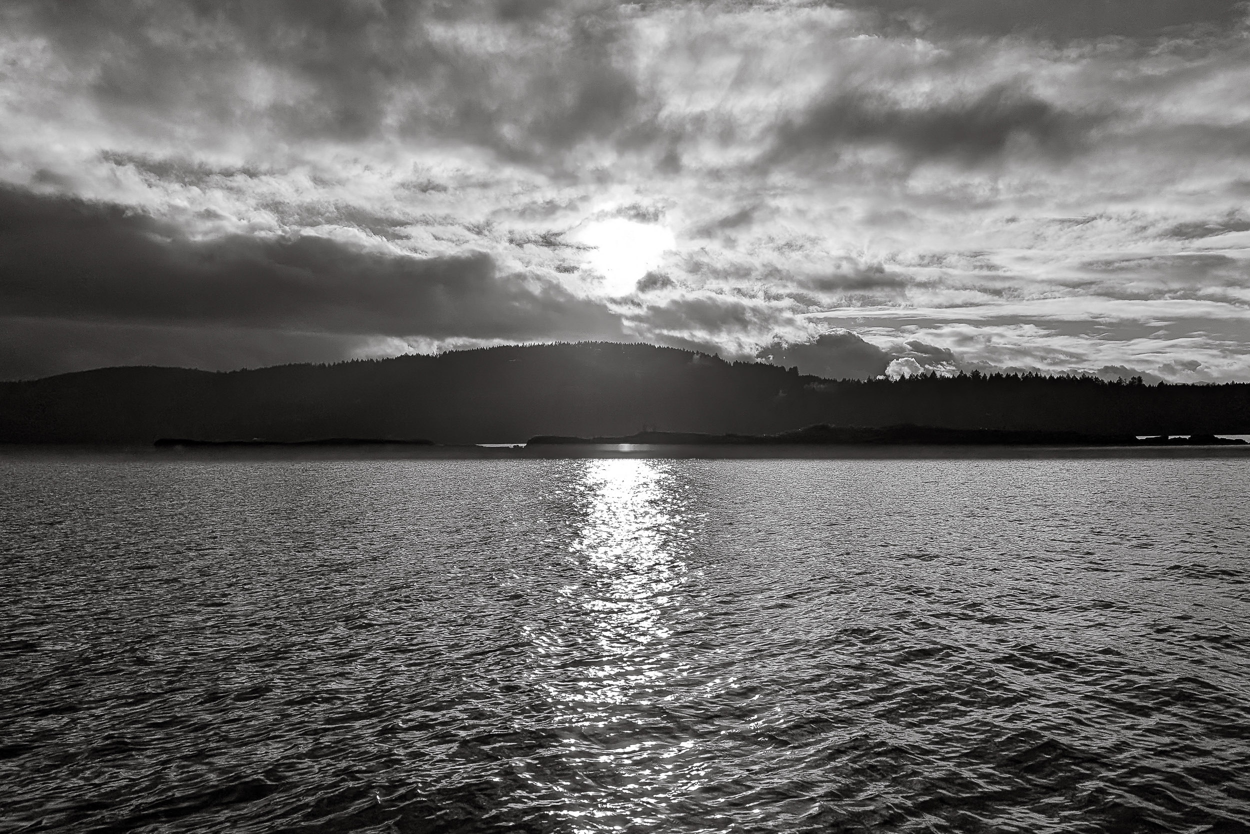 Late light breaks through clouds over rippling water and a distant shore.