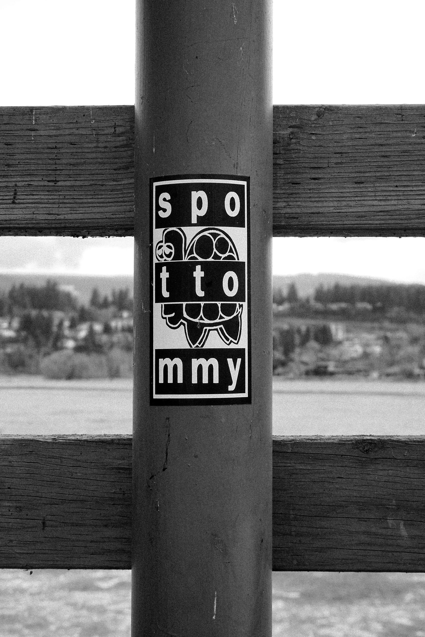 A small stickered sign on a post is framed by an out-of-focus town beyond.