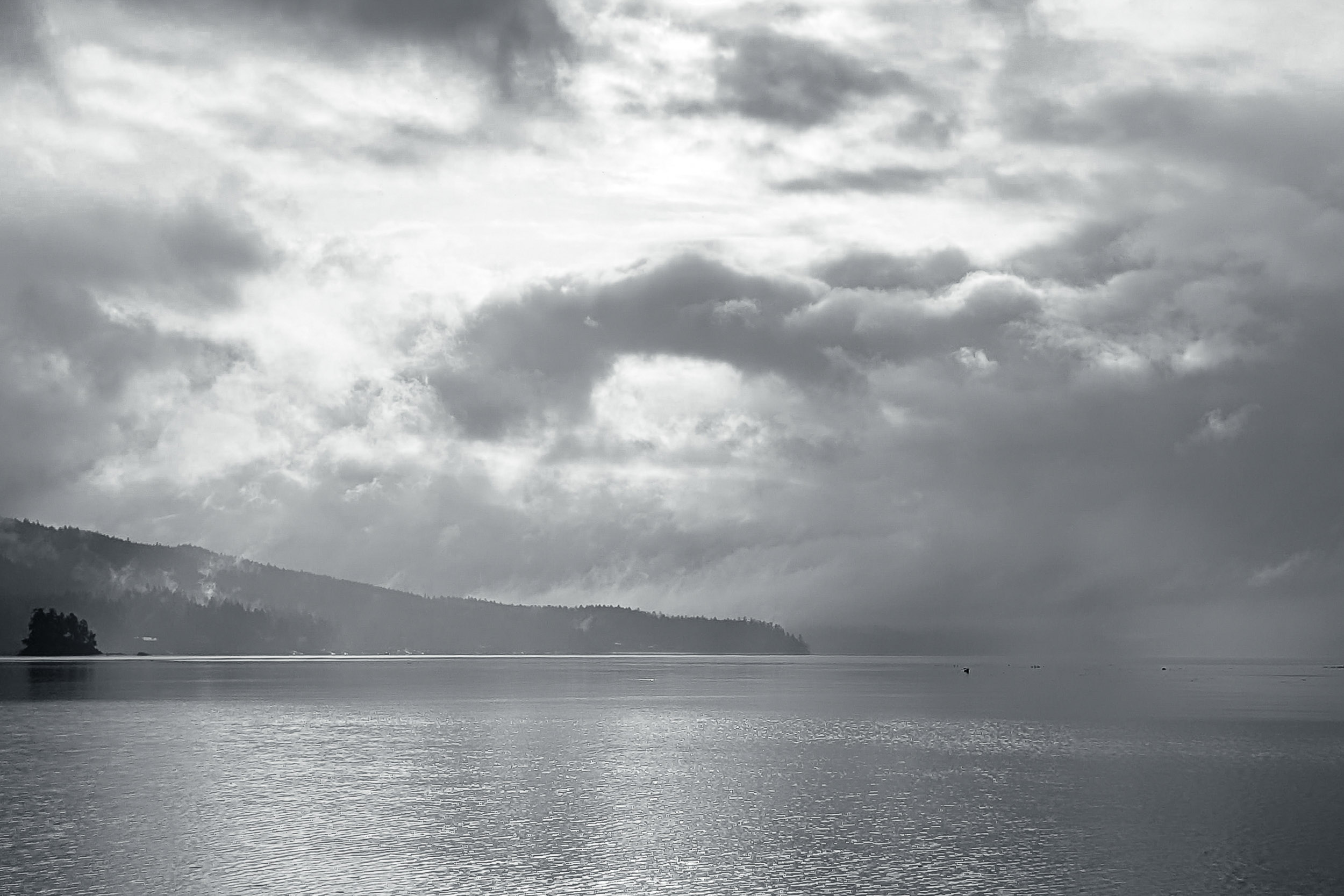 Cloud-filtered light spreads across a wide lake beneath a low horizon.