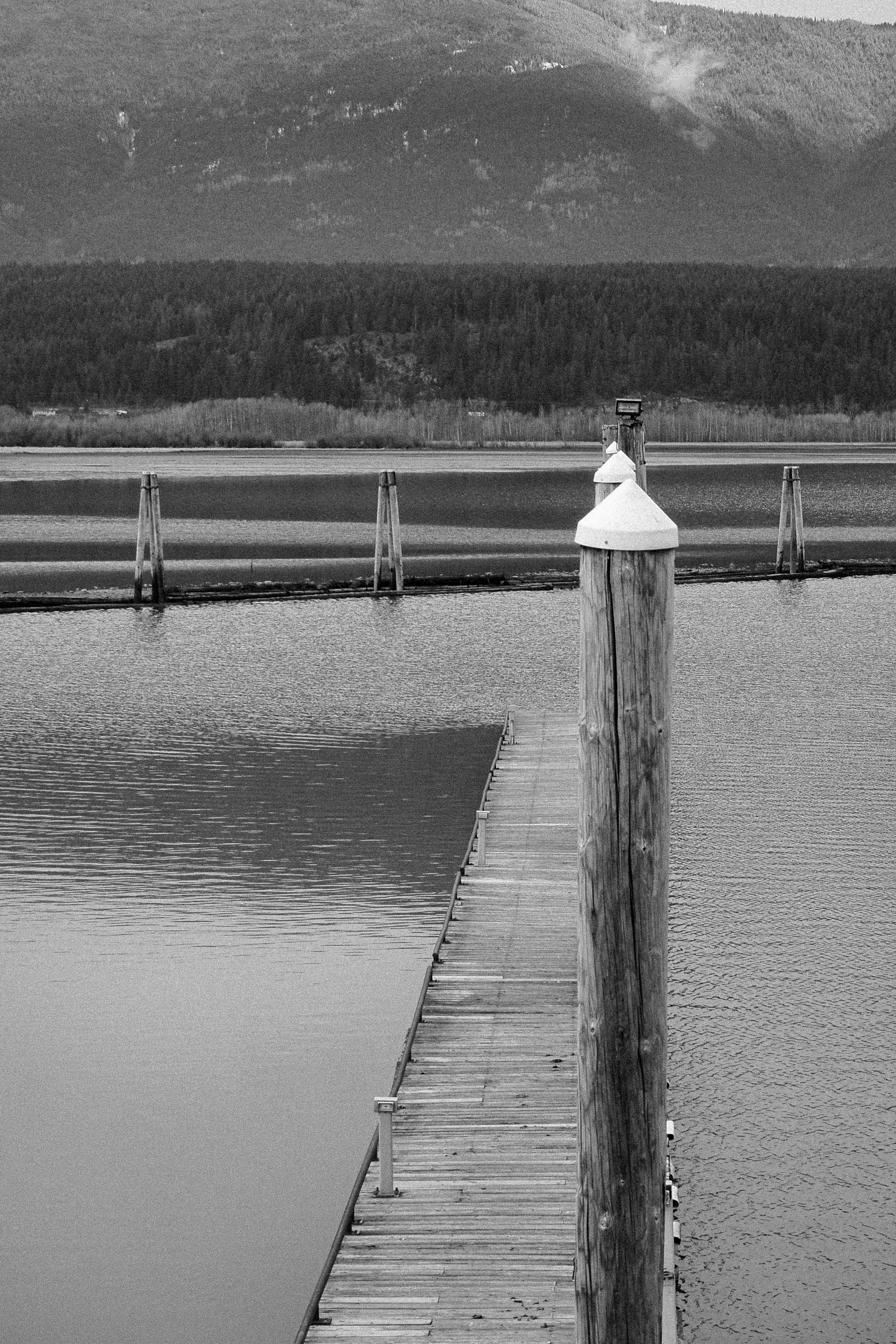 A capped mooring post rises beside a quiet dock and calm water.