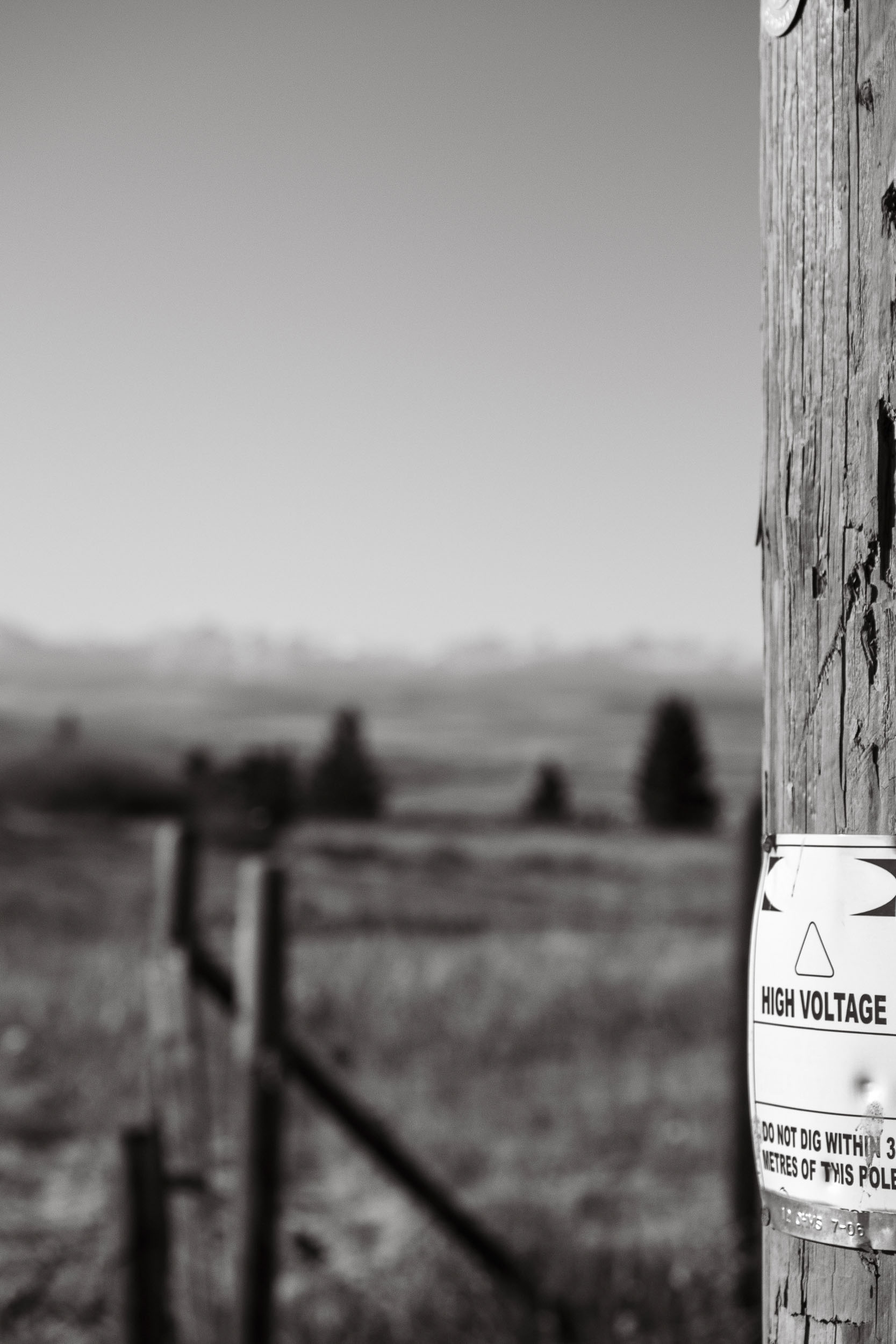 A high-voltage warning label interrupts an out-of-focus rural view.