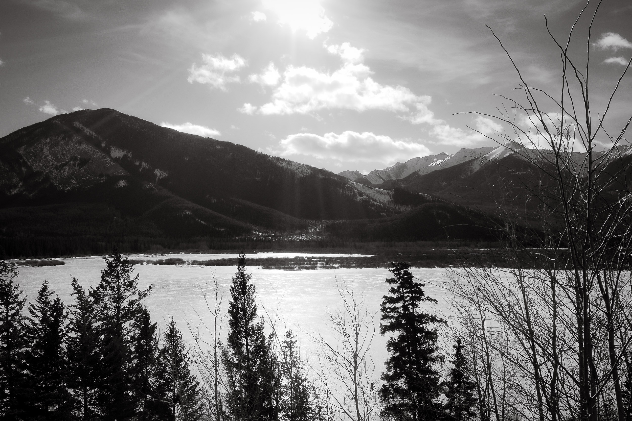 Mountain slopes rise beyond a calm frozen lake under broken clouds.