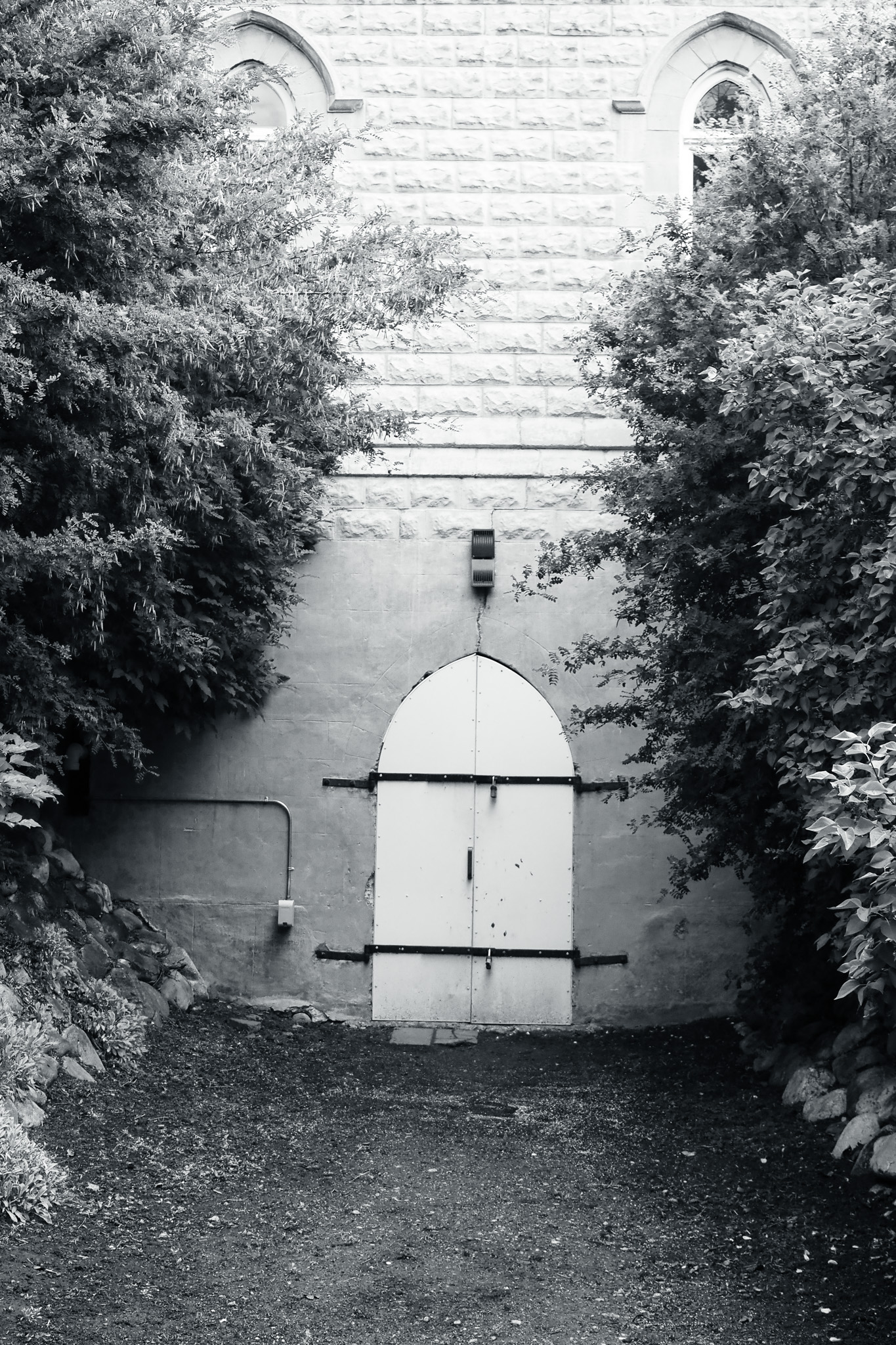A white arched gate is set into a stone wall framed by thick shrubs.